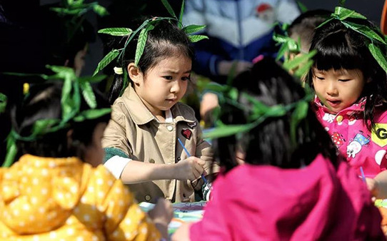 万国城幼儿园的老师带领小朋友们一起编柳条帽，画风筝